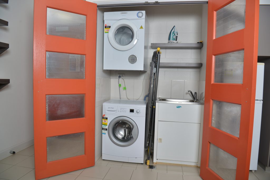 Orange doors opened to show washer, dryer, ironing board and sink