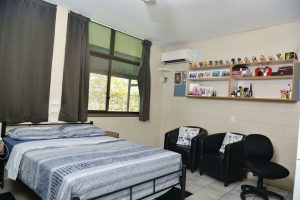 Room with bed, study space and fridge.